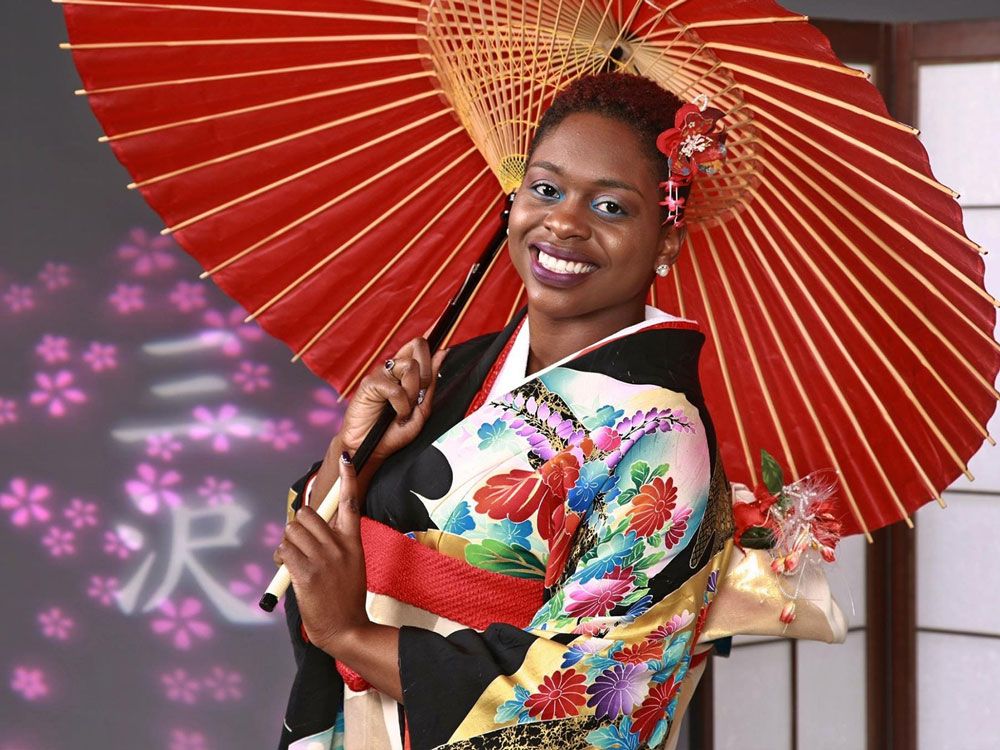 Smiling black woman wearing a colorful traditional Japanese kimono and holding a red umbrella with a red flower in her hair