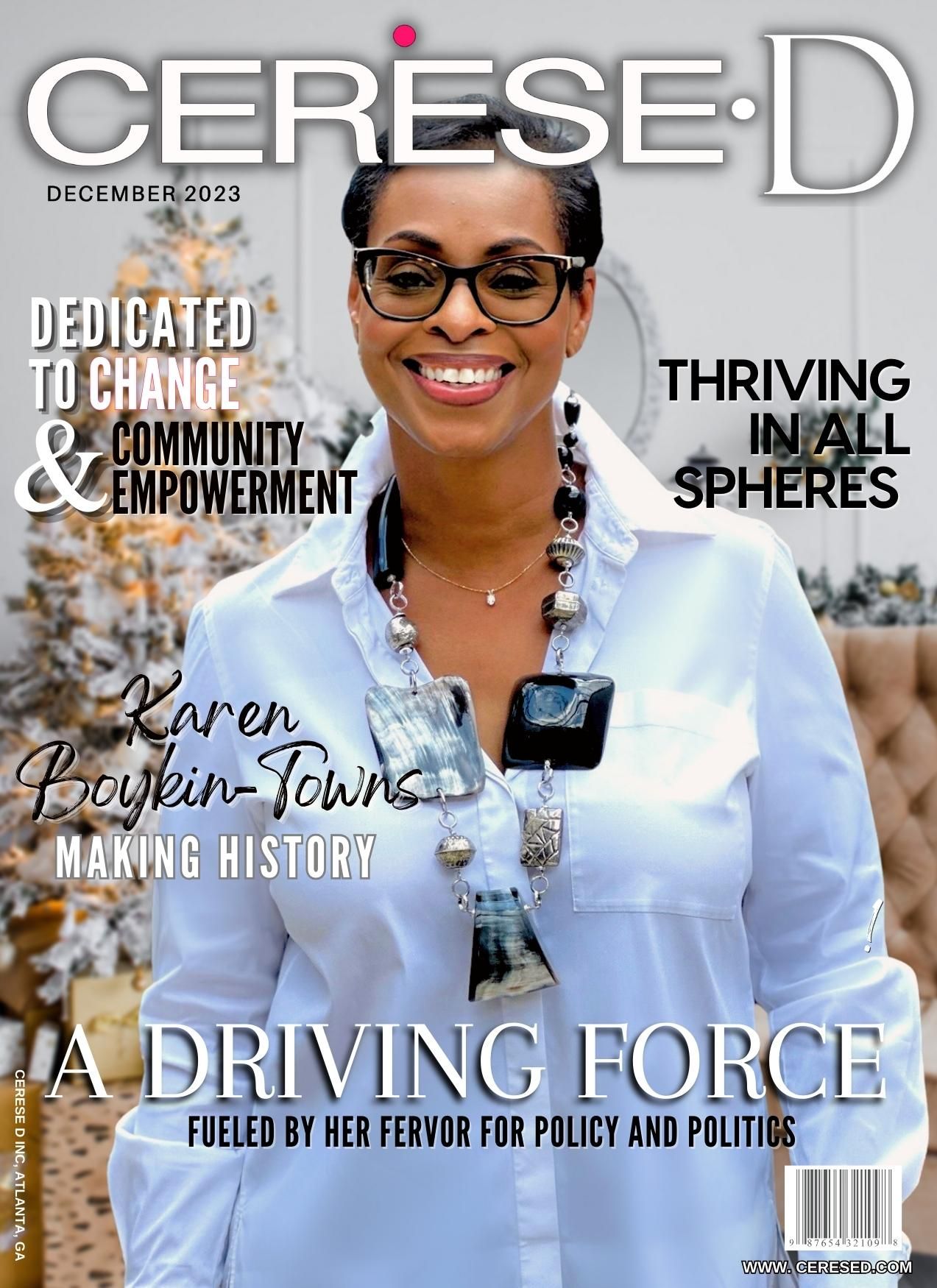 Woman standing in front of a holiday scene with a white christ,as tree in the background smiling with black rimmed glasses and wearing a white button up shirt with a large beaded necklace on a Cerese D magazine cover