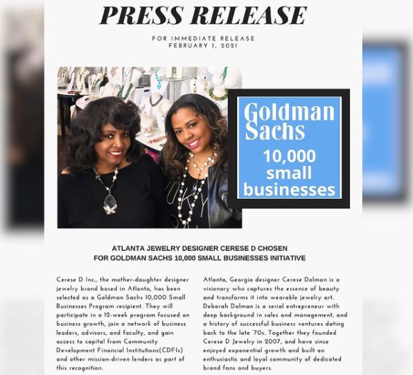 photo of smiling black woman in white top standing in front of a goldman sach 10,000 small business flag