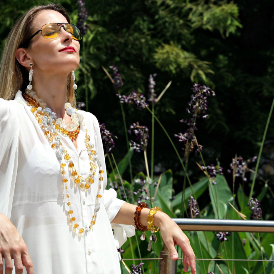 woman in white top basking in sun with long brown beaded layered necklace