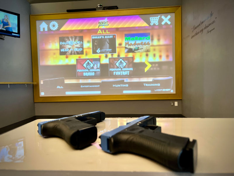 Inside a room at Insight, a Virtual Experience image of two guns in front of a video screen with options to choice from
