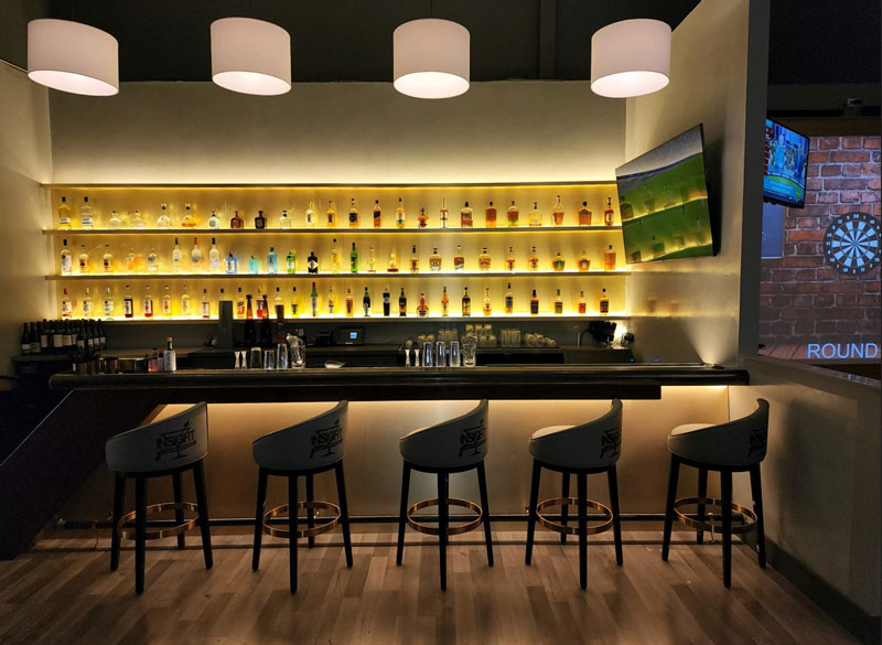 image a bar with bottles of liqueur backlit with yellow lighting and barstools