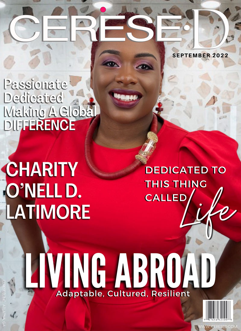Smiling woman wearing a bright red dress and large red coiled necklace with gold accents standing against a white stone facade. on a Cerese D Magazine cover.