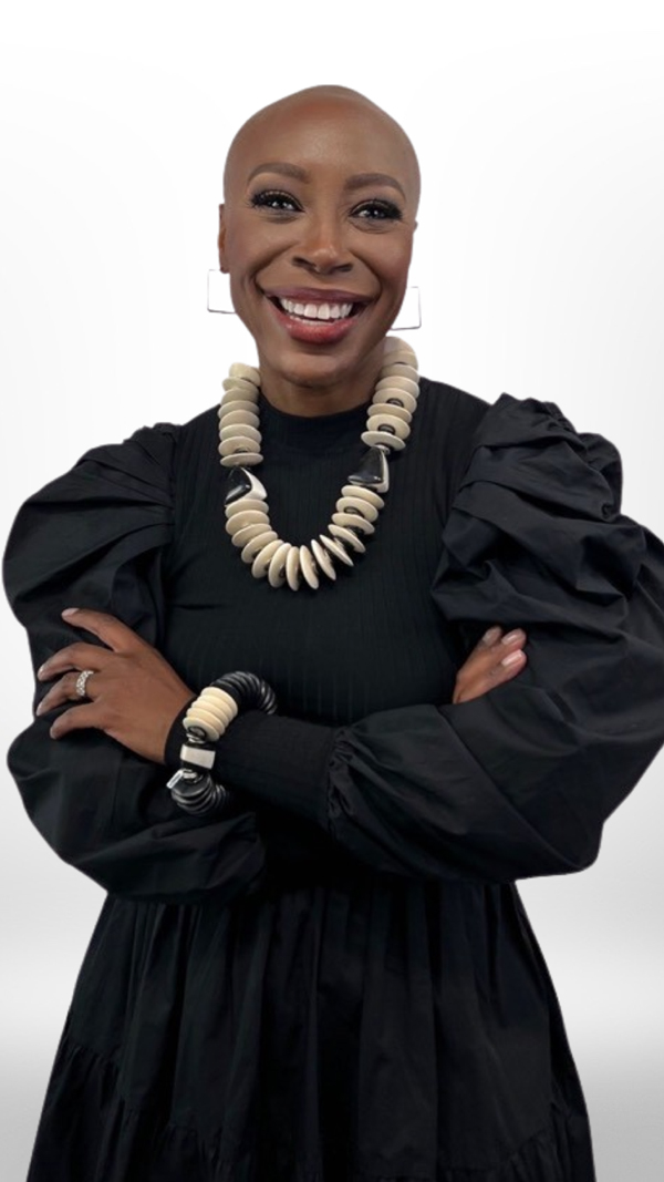 image of smiling black woman wearing a stunning black blouse with wide ruffled sleeves and a large beaded white necklace and matching bracelet standing in front of a white background