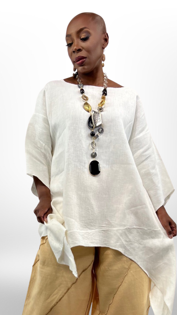 image of a beautiful black woman looking downward wearing a flowing linen white top and tan loose slacks with a large long beaded necklace infront of a white background