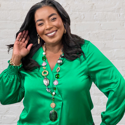 smiling balck woman wearing a bright green button up top and a long large beaded necklace